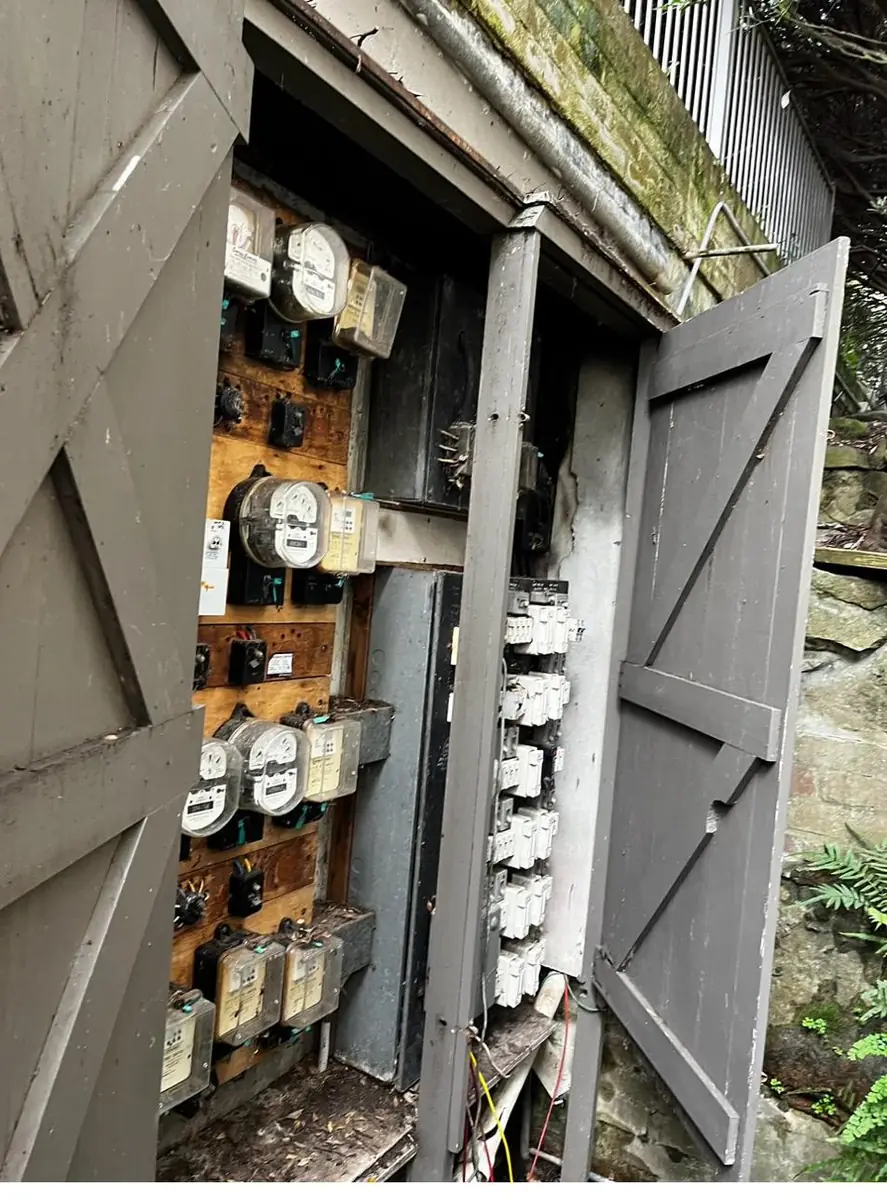 Old timber meter cabinet opened, showing ageing accumulation meters and switchgear on a plywood board
